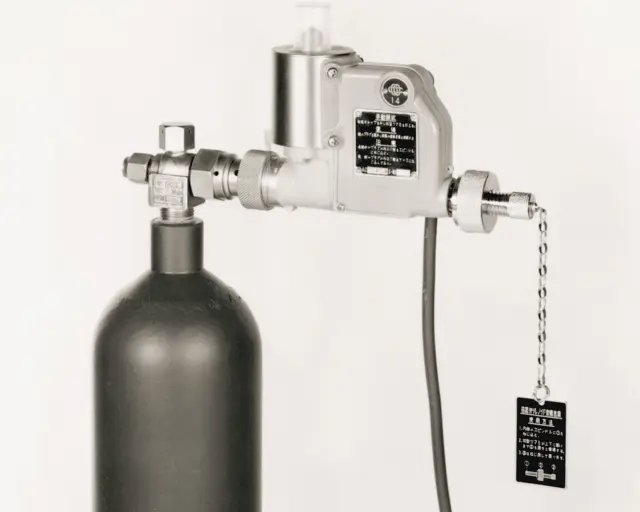 消火用ガスボンベ（容器）の上部に取り付けられた、省電力小型化された消火設備用起動装置または容器弁の写真。